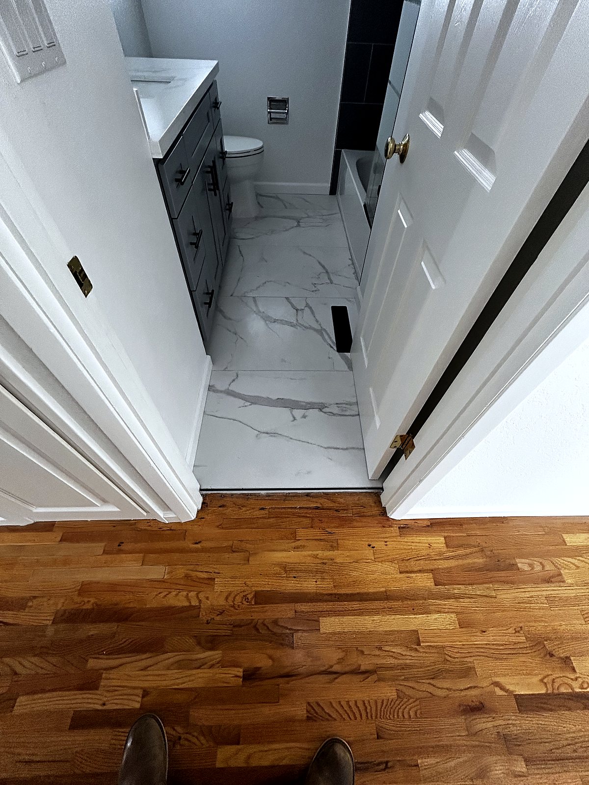 Renovated bathroom with marble-look tile flooring and dark shower surround, King County.